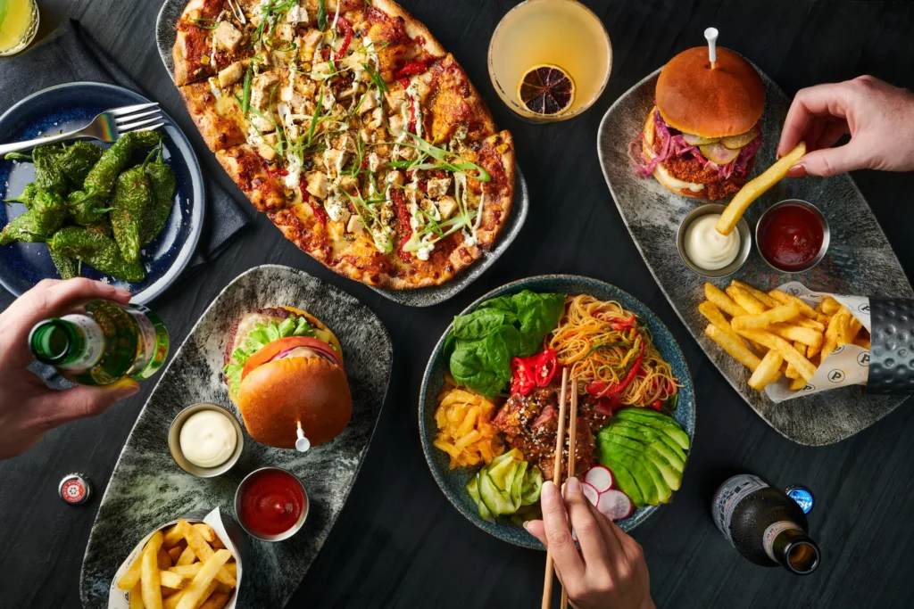 Layout of food and drinks: Peppers, flatbread, burger, asian noodles, pulled pork, and fries