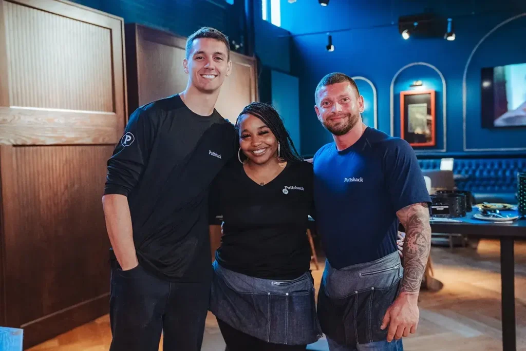 Two male and one female Puttshack employees smiling together