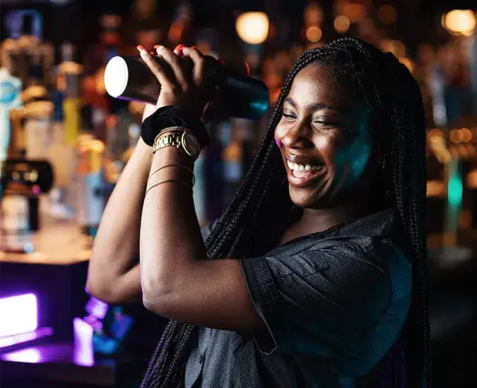 A women smiling and making a mixed drink