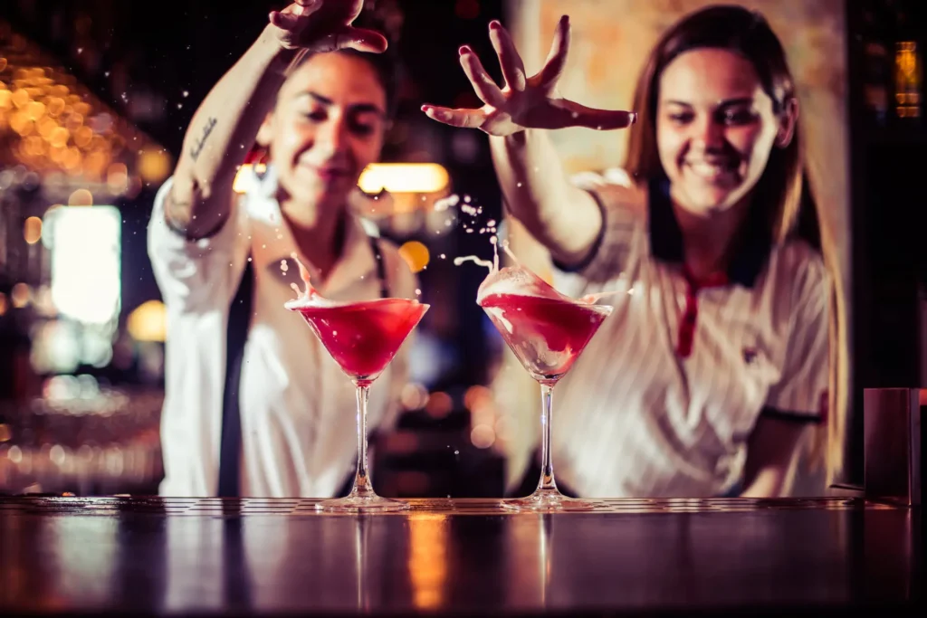 Two women are messing around with two red cocktails