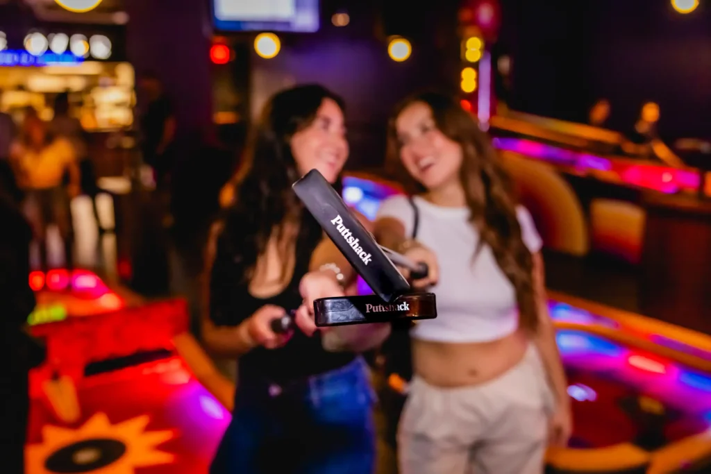Two women holding up putts with the puttshack logo