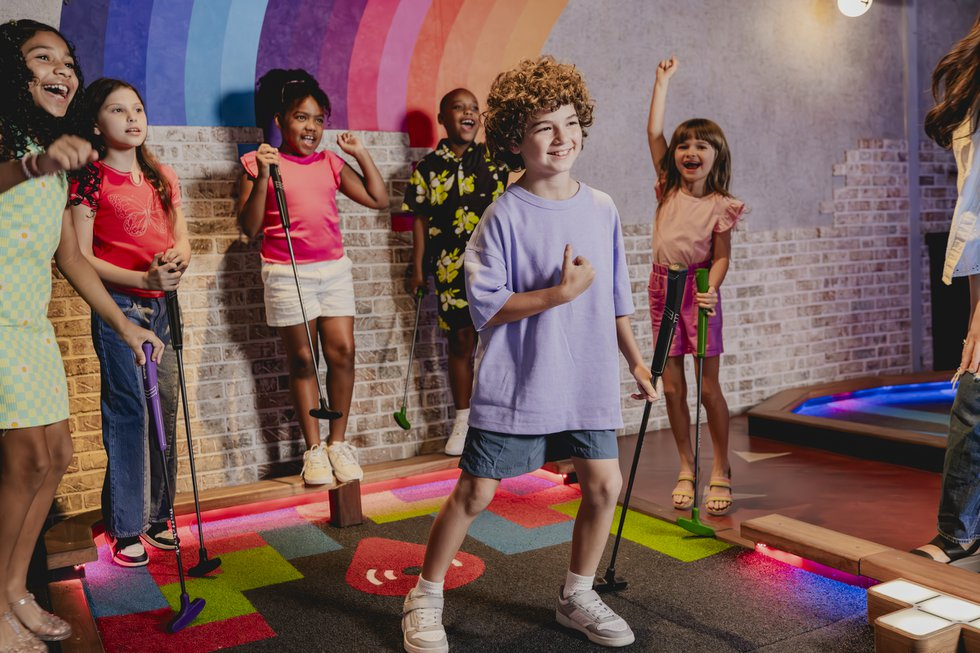 Group of children holding mini golf putters and standing on an indoor mini golf course