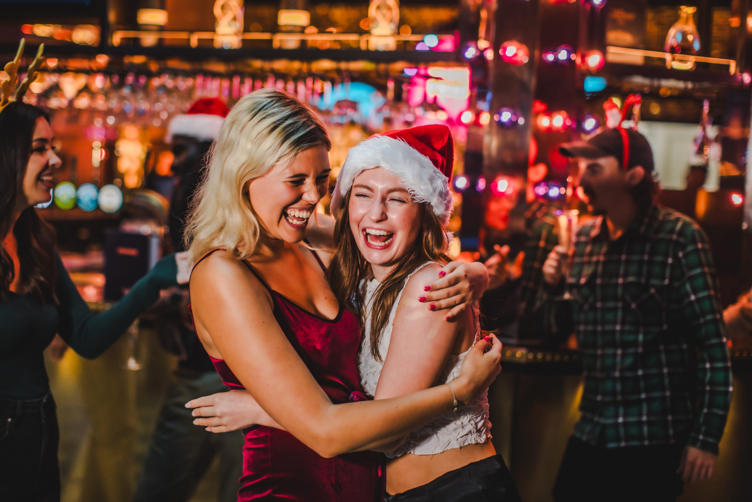 Two woman hugging and laughing in santa hats at Puttshack