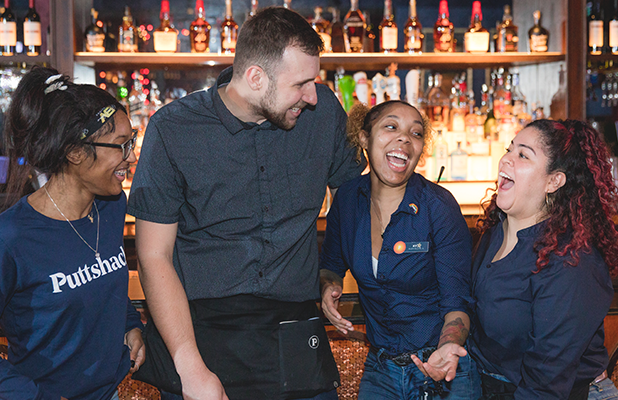 Group of team members standing together and talking behind a bar inside an indoor entertainment venue