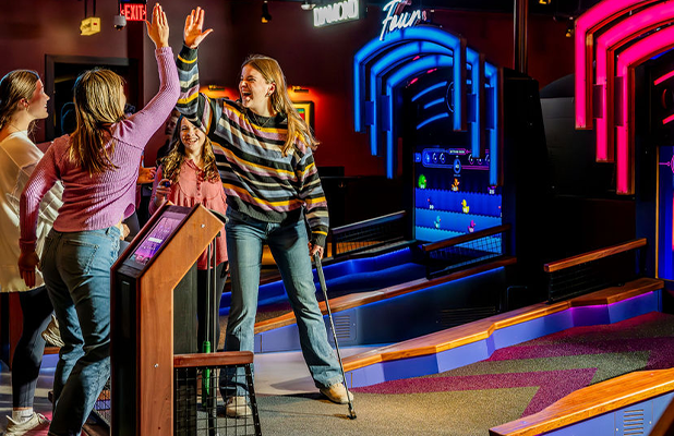 Group of people high‑fiving on an indoor mini golf challenge hole