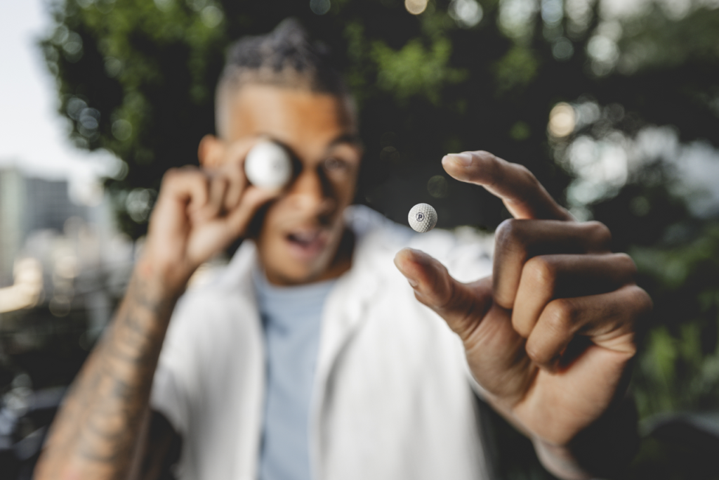 Photo of young adult holding a golf ball up to their eyeball looking at a miniature golf ball