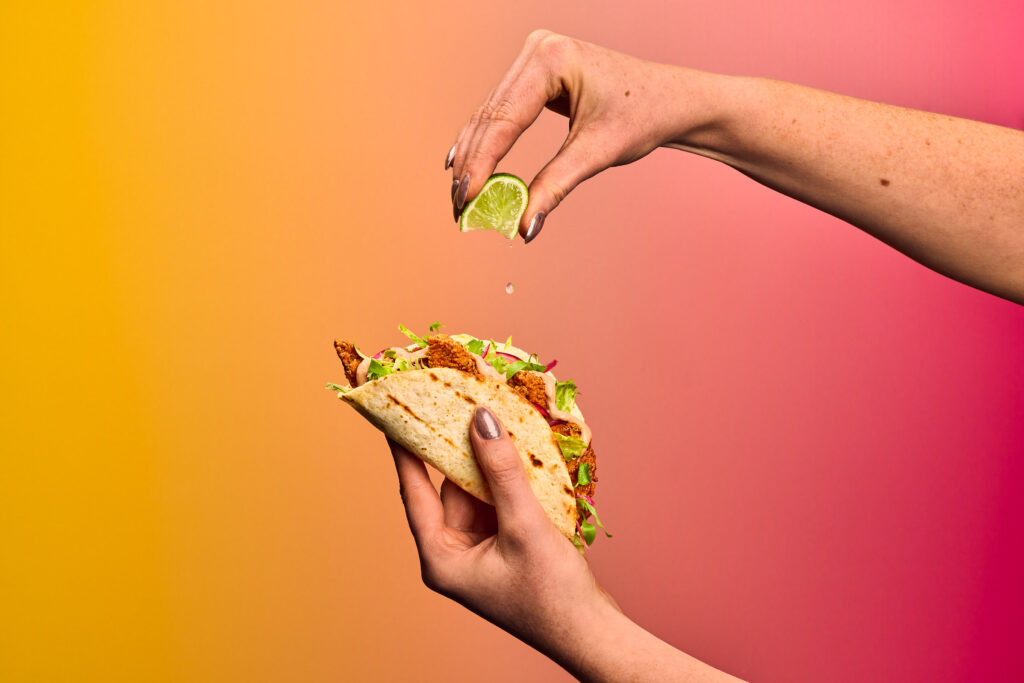 A hand squeezing lime juice onto a chicken taco