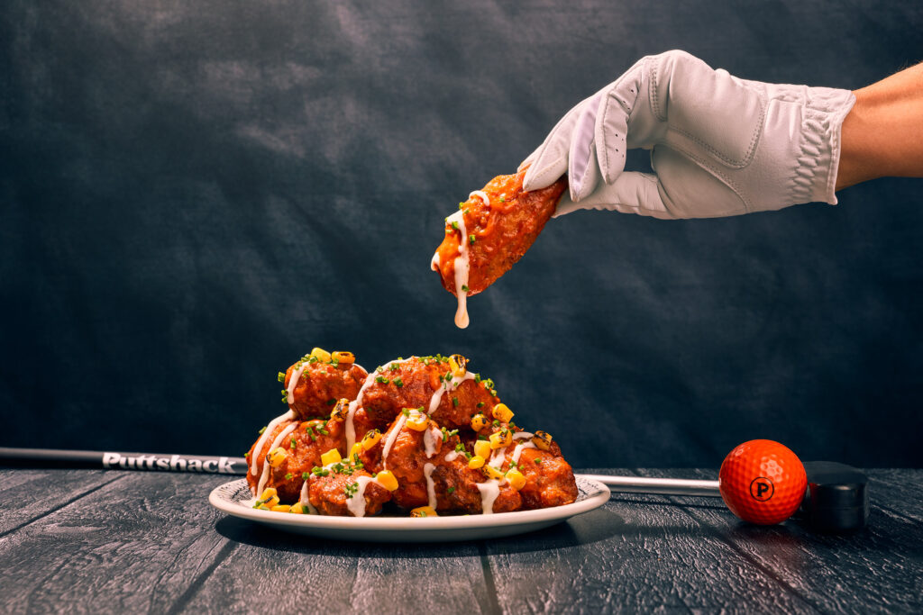 A gloved hand reaching down to pick up a Frank's fiery chicken wing