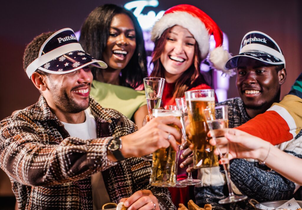 A group of coworkers cheersing their drinks at a work christmas party at puttshack